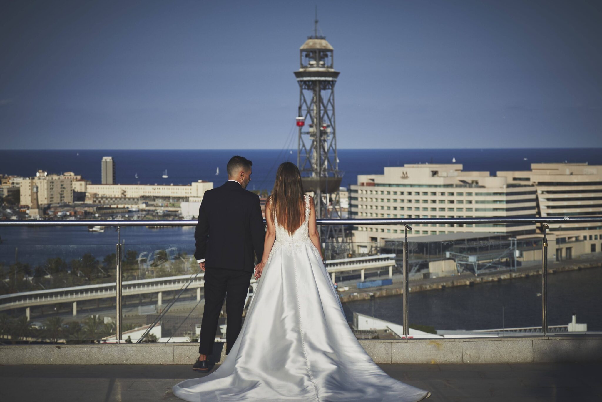 Reportaje de boda exterior con los novios de espaldas contemplando las vistas urbanas frente al mar.