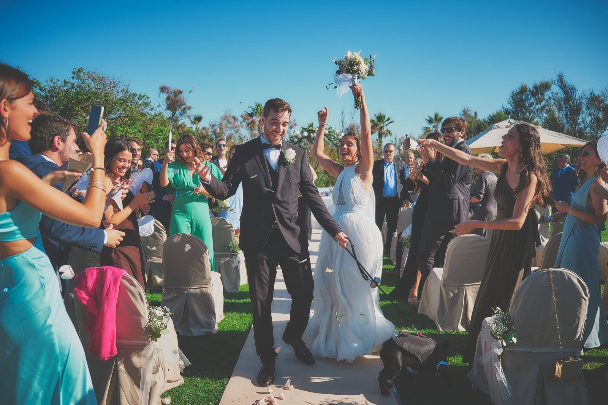 Novios recién casados caminando por el pasillo exterior tras la ceremonia, celebrando con los invitados bajo la lluvia de arroz.